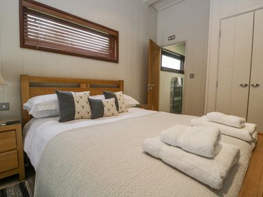 A bedroom with a wooden bed frame white bedding pillows and folded towels at Rivendell Lodge Roger Ground near Hawkshead