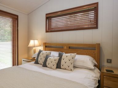 A bedroom with a wooden bed frame pillows with deer print bedside tables and a lamp at Rivendell Lodge in Roger Ground near Hawkshead