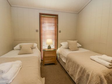 A bedroom with two single beds a wooden nightstand and a window with blinds at Rivendell Lodge Roger Ground near Hawkshead