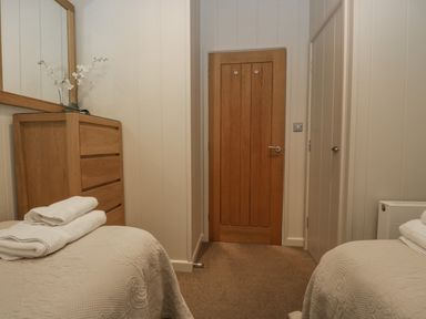 A bedroom with two single beds with folded towels a wooden chest of drawers and a door at Rivendell Lodge Roger Ground near Hawkshead