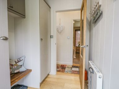 A hallway with white paneled walls a wooden bench with pillows a wooden door opened to a bedroom at Rivendell Lodge Roger Ground near Hawkshead
