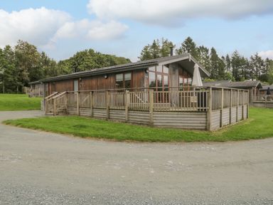 A wooden cabin with a fenced porch and green grass surrounding it at Rivendell Lodge in Roger Ground near Hawkshead
