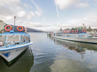 Two boats docked on a lake with hills and trees in the background at Rivendell Lodge Roger Ground near Hawkshead