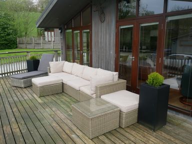 An outdoor deck with wicker furniture including a sofa chaise lounge and table at Rivendell Lodge Roger Ground near Hawkshead