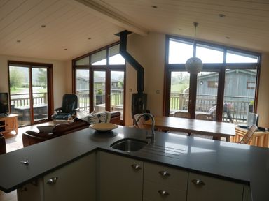 A kitchen island with a sink and faucet overlooking a dining table and living area with large windows and wooden doors at Rivendell Lodge in Roger Ground near Hawkshead