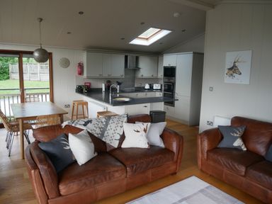 A living room with brown leather sofas and cushions beside a kitchen with cabinets and a dining table at Rivendell Lodge in Roger Ground near Hawkshead