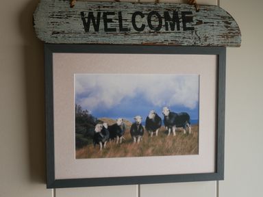A framed picture of five sheep standing on grass under a cloudy sky with a welcome sign above it at Rivendell Lodge Roger Ground near Hawkshead