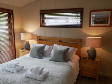 A bedroom with a double bed with two gray pillows and folded towels lit by two bedside lamps at Rivendell Lodge Roger Ground near Hawkshead