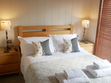A bedroom with a wooden bed frame two pillows two bedside tables lamps and folded towels on a quilted bedspread at Rivendell Lodge Roger Ground near Hawkshead