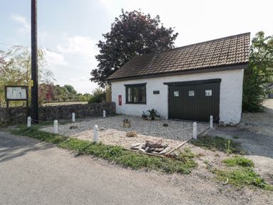 A white building with a black door and window next to a tree and a gravel area at The Forge in Taunton
