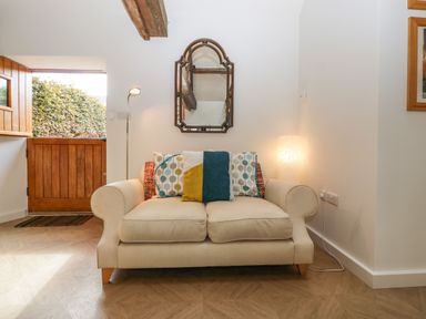 A beige sofa with cushions against a white wall with a decorative mirror above at The Forge in Taunton