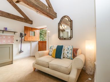 A small sitting area with a beige sofa and colorful cushions under exposed wooden beams at The Forge in Taunton