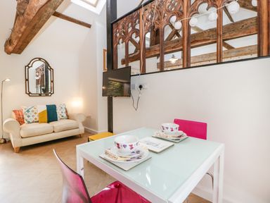 A dining table with two place settings and pink chairs next to a cream sofa with cushions and a wall mirror at The Forge in Taunton
