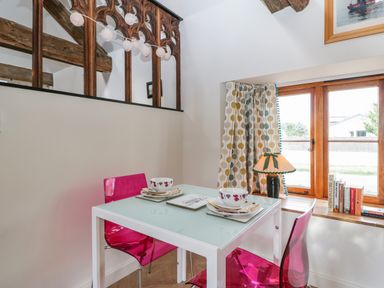 A small dining area with a white table set for two pink chairs a window with curtains a lamp and books on the sill at The Forge in Taunton