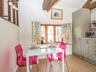 A kitchen dining area with a glass table set for two with pink chairs and a window with patterned curtains at The Forge in Taunton