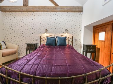A bedroom with a metal bed frame purple bedspread and two teal pillows at The Forge in Taunton