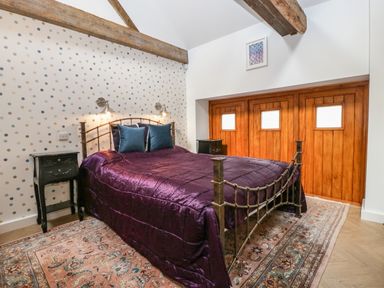 A bedroom with a metal bed frame purple bedspread two black bedside tables a patterned rug and a wooden wardrobe at The Forge in Taunton