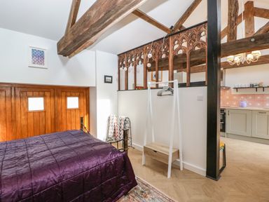 A bedroom with a purple bedspread a wooden divider and kitchen area visible at The Forge in Taunton