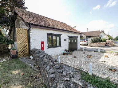 A white stone cottage with a tiled roof and a gravel driveway with potted plants and a red post box at The Forge in Taunton