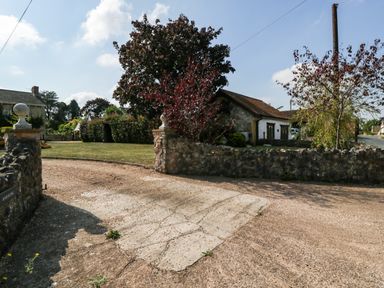 A stone driveway entrance with pillars and a lawn with trees and a house behind a stone wall at The Forge in Taunton