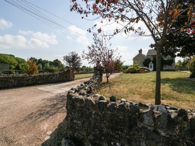 A gravel driveway with stone walls leading to a house with a lawn and trees at The Forge in Taunton