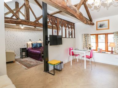 A room with wooden beams a bed with purple bedding a small dining table with two pink chairs and a window with curtains at The Forge in Taunton