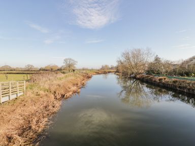 A river with bare trees and grass fields under a blue sky at The Forge in Taunton