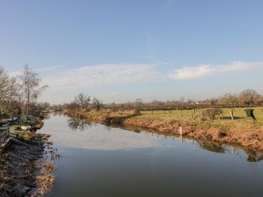 A river bordered by grassy fields and trees under a blue sky at The Forge in Taunton