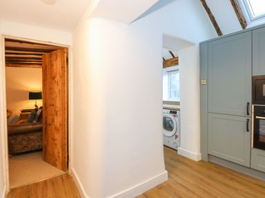 A hallway with white walls and wooden floor leading to a laundry area with a washing machine and kitchen cabinets at Well Cottage in Grimston