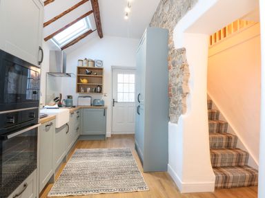 A kitchen with blue cabinets wooden countertops appliances an area rug and a staircase with a plaid carpet at Well Cottage in Grimston