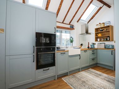 A kitchen with blue cabinets wooden countertop built-in oven microwave farmhouse sink wooden shelves and skylight at Well Cottage in Grimston