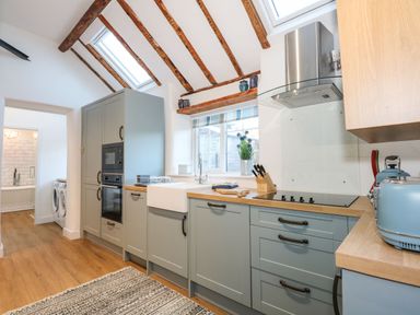 A kitchen with blue cabinets wooden countertops skylights and a washing machine in an adjacent room at Well Cottage in Grimston