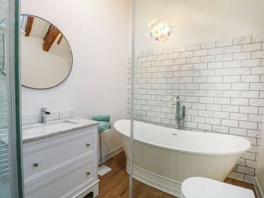 A bathroom with a freestanding bathtub and tiled wall with a round mirror above a sink at Well Cottage in Grimston