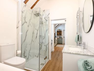 A bathroom with a glass shower, toilet, sink, and a view into a kitchen at Well Cottage in Grimston