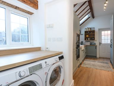 A kitchen with washer and dryer under wooden countertop and kitchen cabinets with appliances and door at Well Cottage in Grimston
