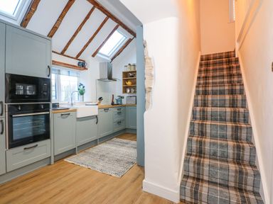 A kitchen with grey cabinets and wooden countertops next to a carpeted staircase at Well Cottage in Grimston