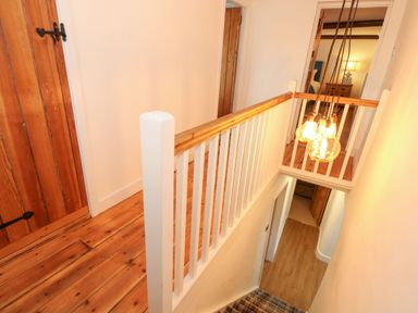 A stairway with a wooden banister leading to a hallway with wooden floors and doors at Well Cottage in Grimston