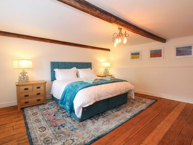 A bedroom with a blue upholstered bed, wooden nightstands with lamps, a patterned rug, and framed pictures on the wall at Well Cottage in Grimston