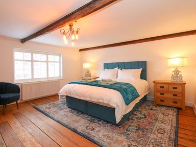A bedroom with a large bed two bedside tables with lamps a window and a chair at Well Cottage in Grimston