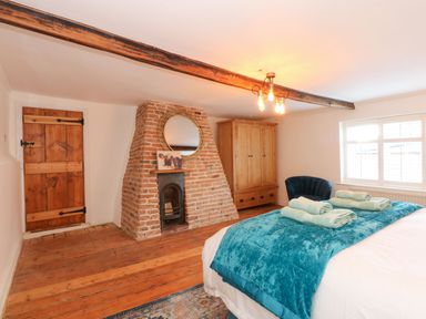 A bedroom with a wooden floor a brick fireplace a wooden wardrobe a blue chair and a bed with folded towels at Well Cottage in Grimston