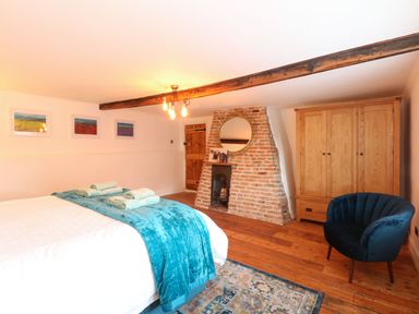 A bedroom with a bed with blue bedding a blue chair a wooden wardrobe and a brick fireplace at Well Cottage in Grimston