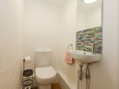 A small bathroom with a toilet sink mirror and mosaic tile backsplash at Well Cottage in Grimston