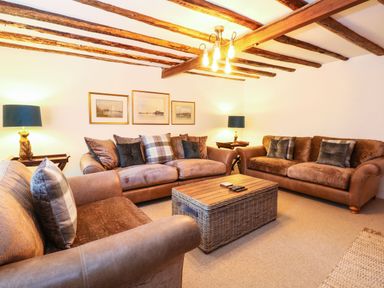 A living room with two brown sofas a wicker coffee table and wooden ceiling beams at Well Cottage in Grimston