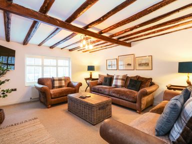 A living room with brown sofas a wicker coffee table wooden ceiling beams and framed pictures on the wall at Well Cottage Grimston