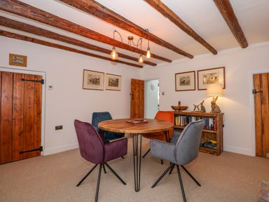 A dining room with a round wooden table and four chairs under exposed wooden beams at Well Cottage in Grimston