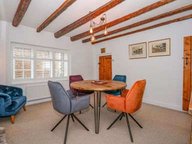 A dining room with a round wooden table surrounded by colorful chairs and exposed wooden ceiling beams at Well Cottage in Grimston