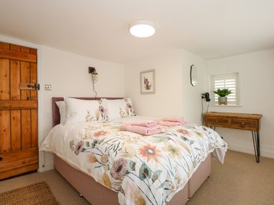 A bedroom with a floral bedspread two folded towels on the bed a wooden door a wooden console table and a small window at Well Cottage in Grimston
