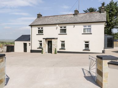 A two-story stone farmhouse with a front door and multiple windows with flower boxes and a paved driveway at Peters Farmhouse in Cookstown