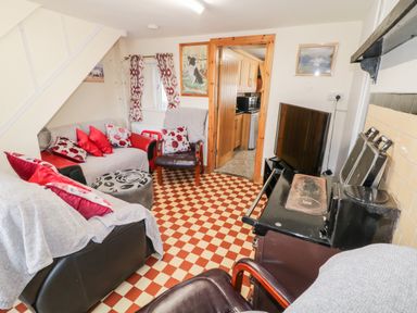 A living room with sofas red and white cushions a black stove a TV and a wooden doorway leading to a kitchen at Peters Farmhouse in Cookstown