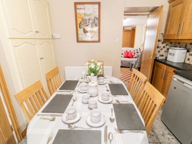A kitchen dining area with a table set with cups and cutlery wooden chairs cabinets and a door leading to a living room at Peters Farmhouse in Cookstown